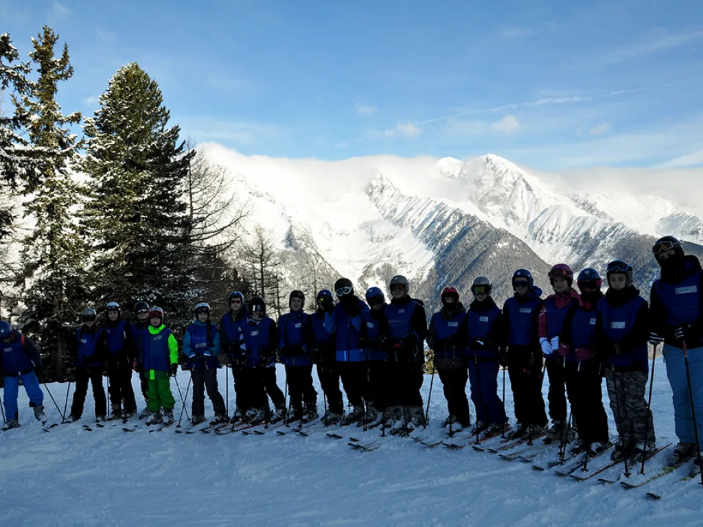 Skigruppe steht in einer Reihe vor Lärchen und Gipfeln.